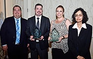Photo of two men and two women posing for a group picture. The man and woman in the center are holding awards.