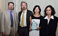 Photo of two men and two women posing for a group picture. The woman in the center is holding an award.