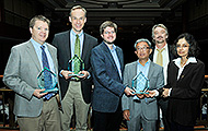 Photo of five men and one woman posing for a group picture. Three of the men are holding awards.