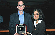 Photo of one man and one woman posing for a picture. The man is holding an award.