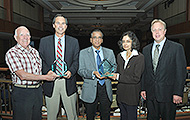 Photo of four men and one woman posing for a group picture. Two of the men are holding awards.