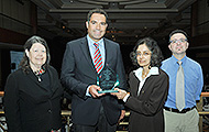 Photo of two men and two women posing for a group picture. One of the men is holding an award.