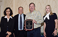 Photo of two women and two men posing for a group picture. One man in the center is holding an award.