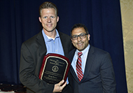 Photo of two men posing for a picture. One of the men is holding an award.