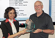 Photo of one woman and one man posing for a picture. The man is holding an award.