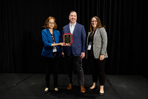 Three people stand with an award plaque.