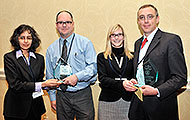 Photo of two men and two women posing for a group picture. The two men are holding awards.