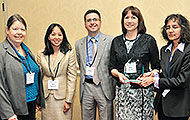 Photo of four women and one man posing for a group picture. One of the women is holding an award.