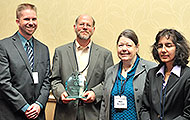 Photo of two men and two women posing for a group picture. One of the men is holding an award.